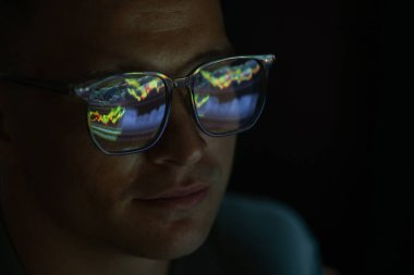 Siyah arka planda yansıması olan gözlüklü genç adam, yakın plan.