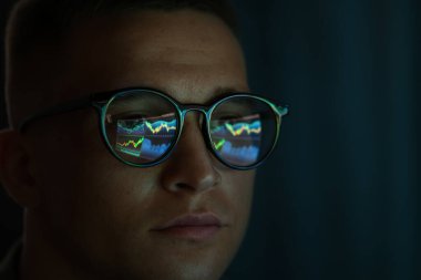 Siyah arka planda yansıması olan gözlüklü genç adam, yakın plan.