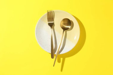 Sarı arka planda şık tabak ve çatal bıçak takımı, üst görünüm