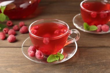 Cam bardaklarda ahududu çayı, ahşap masada nane ve böğürtlen, yakın plan.