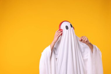 Turuncu arka planda kulaklık takan hayalet kostümlü bir adam. Metin için boşluk