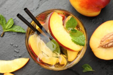 Buzlu şeftali çayı bardakta ve taze meyveler koyu masada, düz yerde.