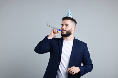 Doğum günün kutlu olsun. Gri arka planda parti şapkası ve üflemeli yakışıklı bir adam.