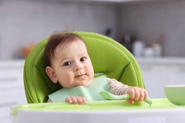 Evdeki beslenme sandalyesinde yemek yiyen şirin bir bebek.