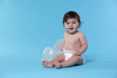 Açık mavi arka planda lazımlığın yanında oturan sevimli küçük bebek.