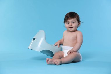 Açık mavi arka planda lazımlığın yanında oturan sevimli küçük bebek.