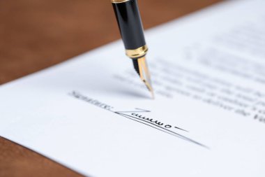 Kahverengi masadaki dolma kalemle noter belgesi imzalanırken, yakın plan