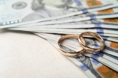 Beyaz masada iki altın alyans ve bir dolarlık banknotlar, yakın plan. Metin için boşluk