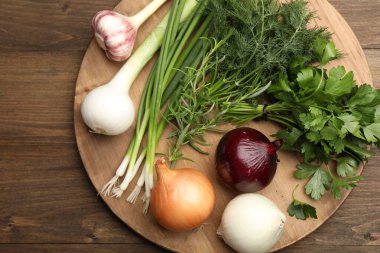 Farklı taze otlar, soğanlar ve sarımsak, ahşap masa, üst manzara.