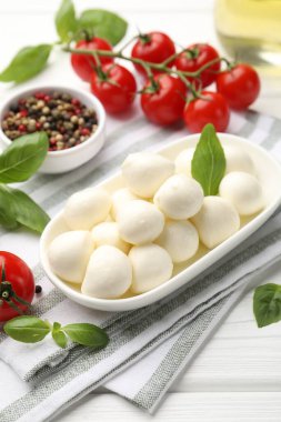 Lezzetli mozzarella peyniri, domates, fesleğen ve baharatlar beyaz ahşap masada, yakın plan.