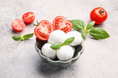Lezzetli mozzarella peynir topları, domates ve fesleğen gri masada, yakın plan.