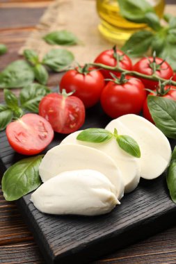Lezzetli mozzarella peyniri, domates ve fesleğen ahşap masada, yakın plan.