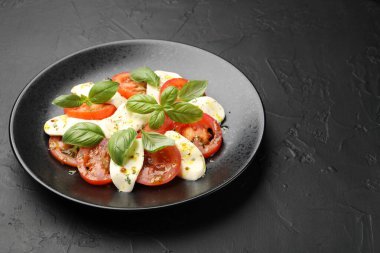Peynirli Caprese salatası, domates, fesleğen ve baharatlar siyah masada, yakın plan. Metin için boşluk