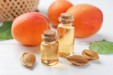 Beyaz ahşap masa üzerinde gerekli yağ şişeleri, taze kayısılar ve çekirdekler, yakın plan.