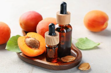 Açık gri masada gerekli yağ şişeleri, taze kayısılar, çekirdekler ve yeşil yapraklar, yakın plan.