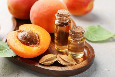 Açık gri masada gerekli yağ şişeleri, taze kayısılar, çekirdekler ve yeşil yapraklar, yakın plan.