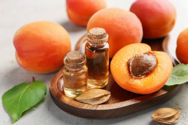 Açık gri masada gerekli yağ şişeleri, taze kayısılar, çekirdekler ve yeşil yapraklar, yakın plan.