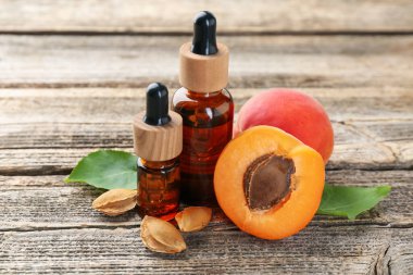 Kaliteli yağ şişeleri, taze kayısılar, çekirdekler ve ahşap masa üzerindeki yeşil yapraklar, yakın plan.