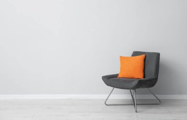 Açık gri duvarın yanında rahat bir koltuk ve turuncu yastık. Metin için boşluk