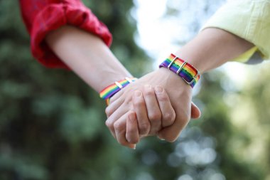 LGBT konsepti. Gökkuşağı bileklikli kadınlar dışarıda el ele tutuşuyorlar, yakın plan.