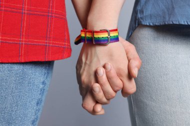 LGBT konsepti. Gökkuşağı bileklikli kadınlar açık gri arka planda el ele tutuşuyorlar, yakın plan.