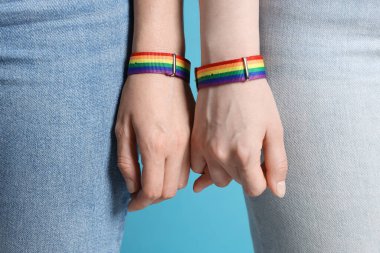 LGBT konsepti. Gökkuşağı bileklikli kadınlar açık mavi arka planda el ele tutuşuyorlar, yakın plan.