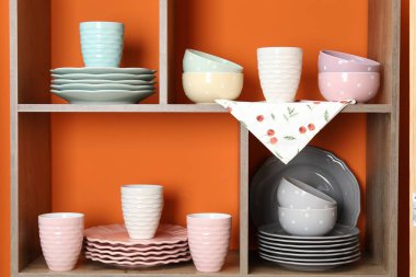 Kapalı alanda turuncu duvarın yanında farklı bulaşık takımları ve fincanlar olan raf ünitesi.