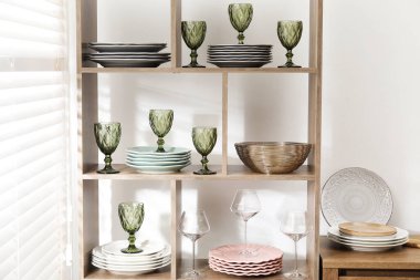 Beyaz duvarın yanında farklı bulaşık takımları ve gözlüklerle raf ünitesi.