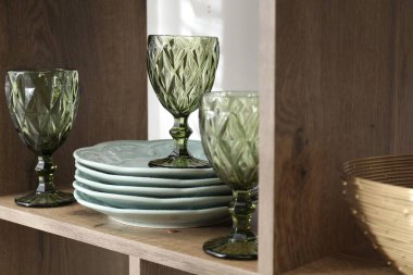 Kapalı alanda, ahşap rafta farklı tabaklar ve bardaklar var.