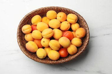 Taze kayısılar hasır sepetin içinde beyaz mermer masanın üstünde, üst tarafta.