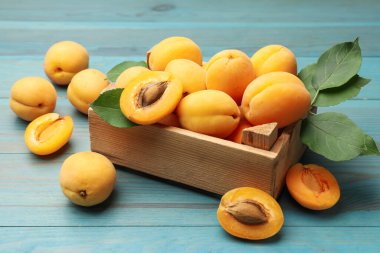 Açık mavi ahşap masada sandıkta lezzetli olgun kayısılar, yakın plan.