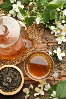 Aromatik yasemin çayı cam fincanda, çaydanlıkta, demlikte ve çiçeklerde ahşap masada, düz yerde.