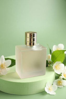 Yeşil arka planda bir şişe parfüm ve yasemin çiçeği, yakın plan.