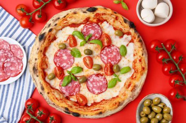 Lezzetli pizza ve malzemeler kırmızı masada, düz yerde.