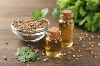 Şişe içinde Aromatik yağ, kişniş yaprakları ve ahşap masa üzerinde kişniş tohumları, yakın çekim