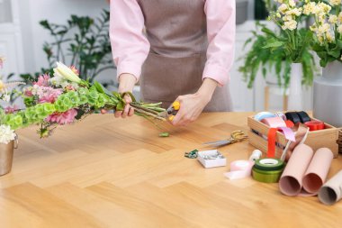 Dükkandaki ahşap masada çiçek buketi yapan profesyonel bir çiçekçi.