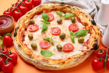 Turuncu arka planda servis edilen domatesli, fesleğenli ve zeytinli lezzetli pizza.