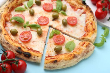 Açık mavi arka planda domatesli, fesleğenli ve zeytinli pizza, yakın plan.