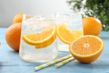 Portakal dilimli maden suyu, taze meyve ve pipetler açık mavi ahşap masada, yakın plan.