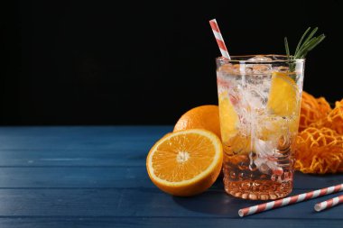 Bardakta portakallı maden suyu, mavi ahşap masada taze meyve ve pipetler, yakın plan. Metin için boşluk