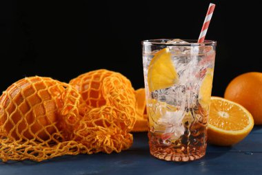 Bardakta portakallı köpüklü su ve mavi ahşap masada taze meyveler, yakın plan.