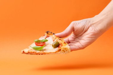 Turuncu arka planda lezzetli bir pizza dilimi tutan kadın, yakın plan.
