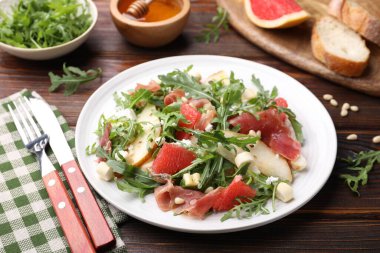 Lezzetli salata roka, prosciutto, peynir, armut, greyfurt ve ahşap masada fındık, yakın plan.