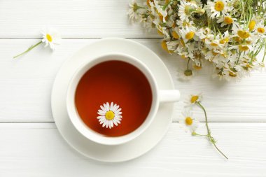 Aromatik çay fincanda ve papatya çiçekleri beyaz ahşap masada, düz yatıyordu.