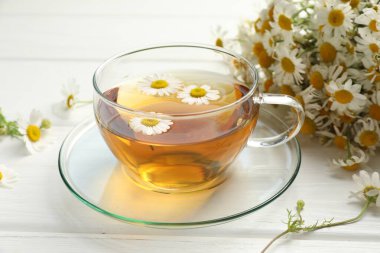 Cam bardakta Aromatik çay ve beyaz ahşap masada papatya çiçekleri, yakın plan.