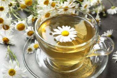 Lezzetli papatya çayı ve çiçekler gri masada, yakın plan.