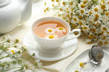 Lezzetli papatya çayı, zerk makinesi ve çiçekler beyaz ahşap masada, yakın plan.