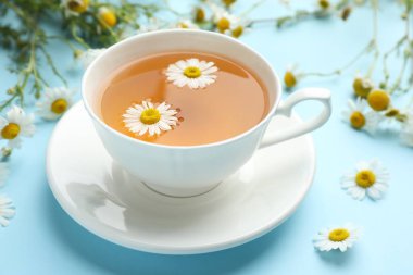 Lezzetli papatya çayı ve açık mavi arka planda çiçekler, yakın plan.