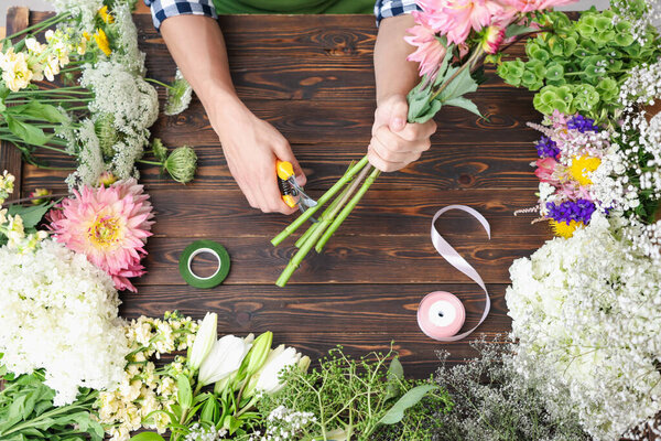 Профессиональный флорист делает букет цветов за деревянным столом, вид сверху