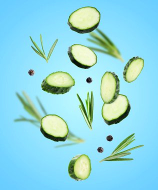 Salatalık dilimleri, biberiye ve biber taneleri açık mavi arka plana düşüyor.